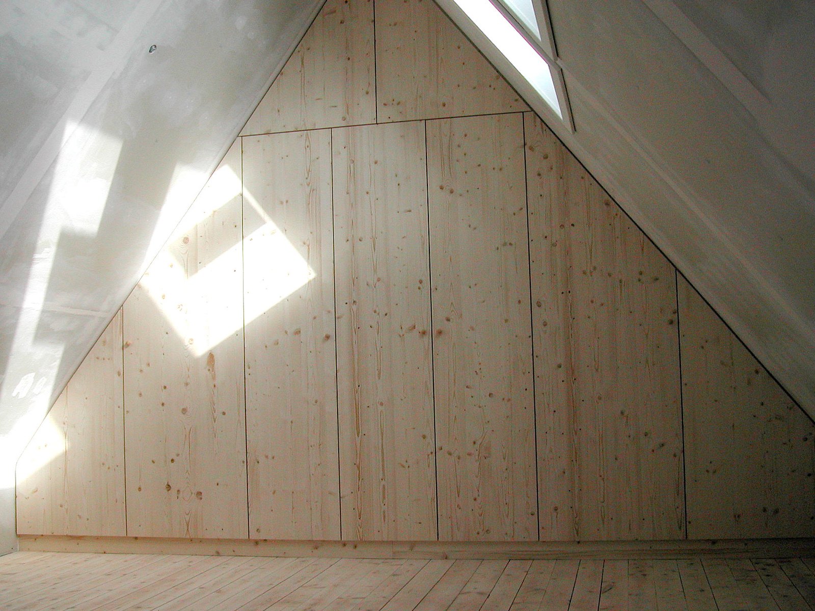 Raumhoher Einbauschrank mit hellen Holztüren, passgenau in eine Dachschräge mit Dachfenster eingepasst