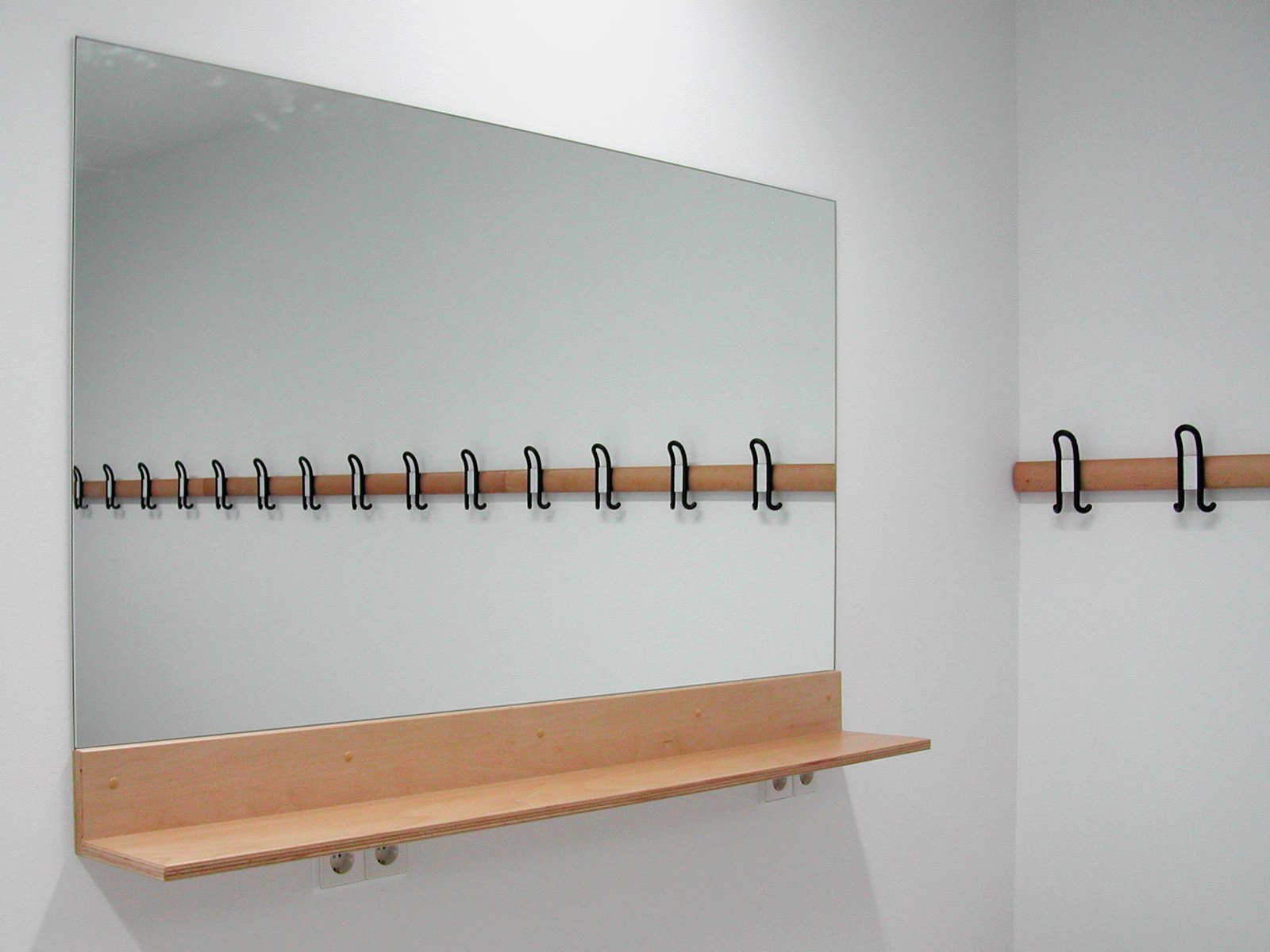 Garderobe mit langer Hakenleiste, Holzablage und großem Spiegel an einer weißen Wand